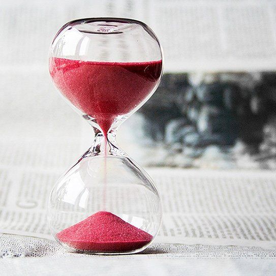 A hourglass filled with red sand is sitting on top of a newspaper.