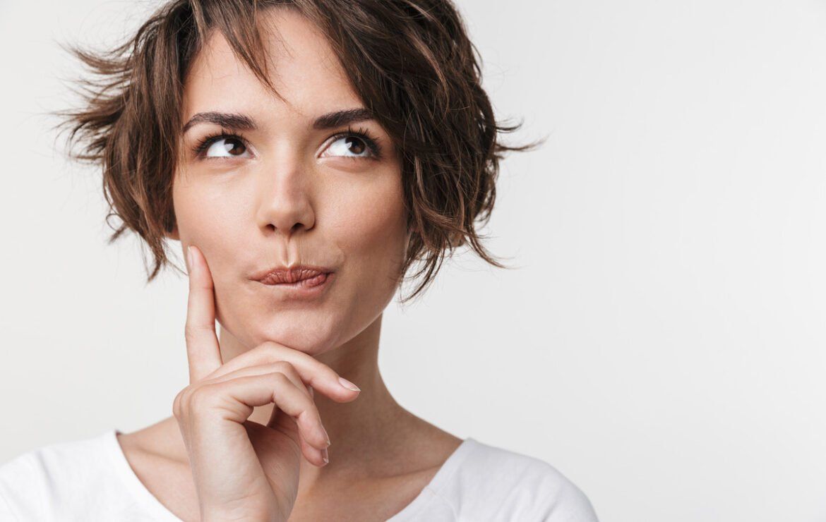 A woman with short hair is holding her hand to her chin and looking up.