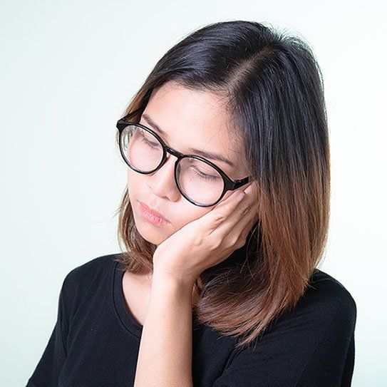 A woman wearing glasses is holding her hand to her face.
