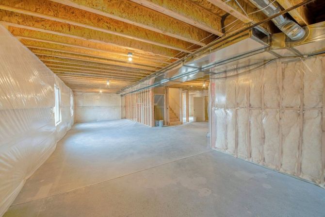 Unfinished basement with insulated walls, exposed wood beams, and concrete floor