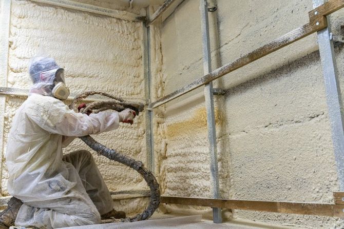 Worker spray-applies insulation foam to a wall inside a construction space