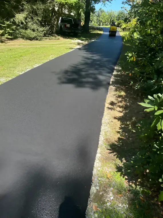 A freshly paved black asphalt driveway stretches into the distance, with a steamroller visible in the background.