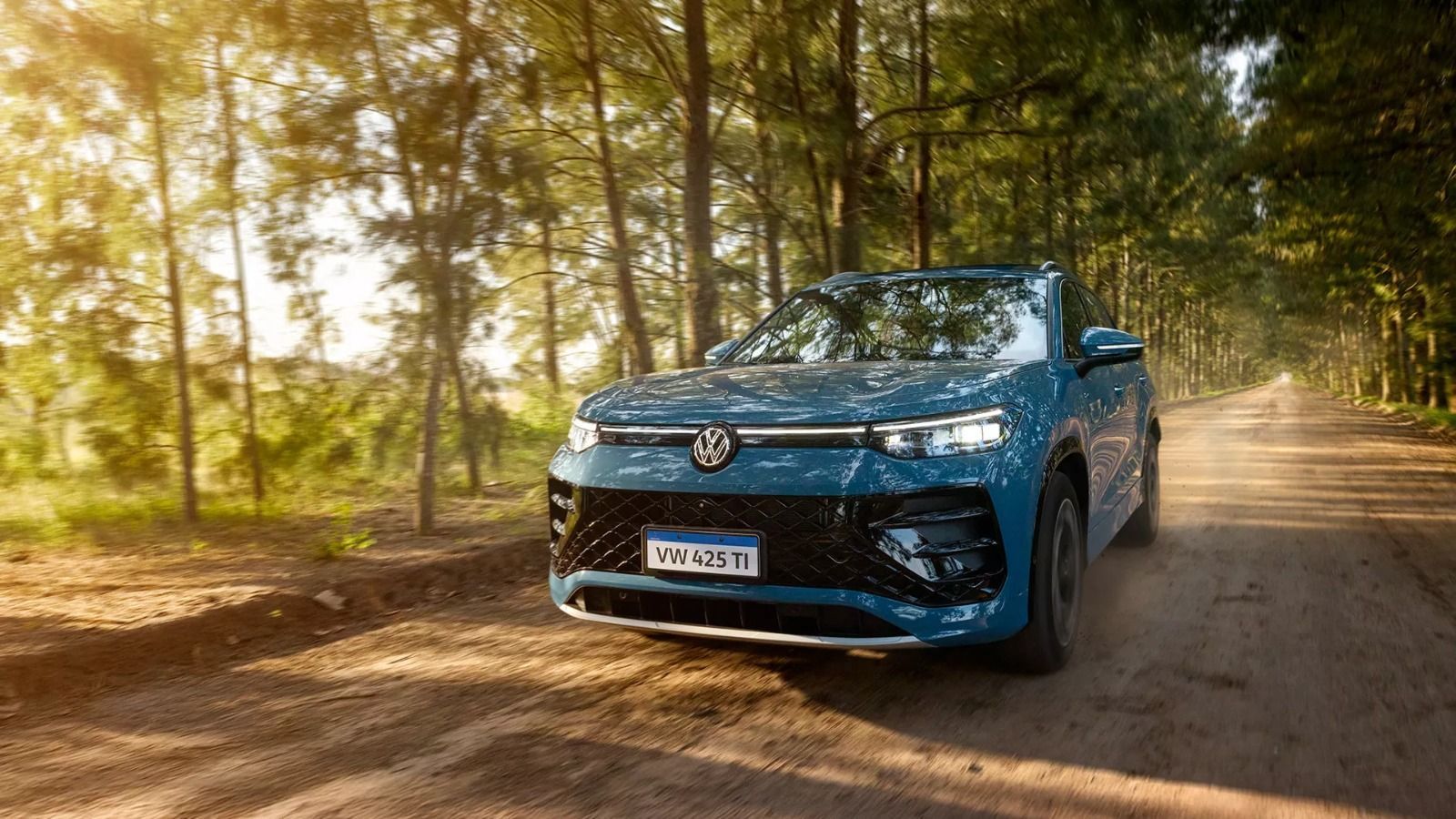 SUV azul trafegando por uma estrada de terra em meio a uma floresta ensolarada.