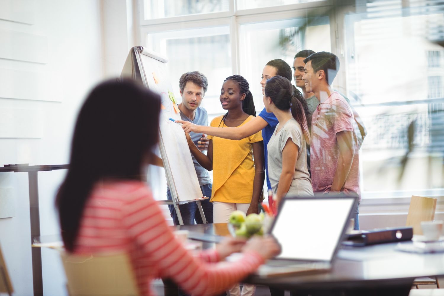 Team in a bright office collaborating around a whiteboard while one person sits at a laptop in the foreground