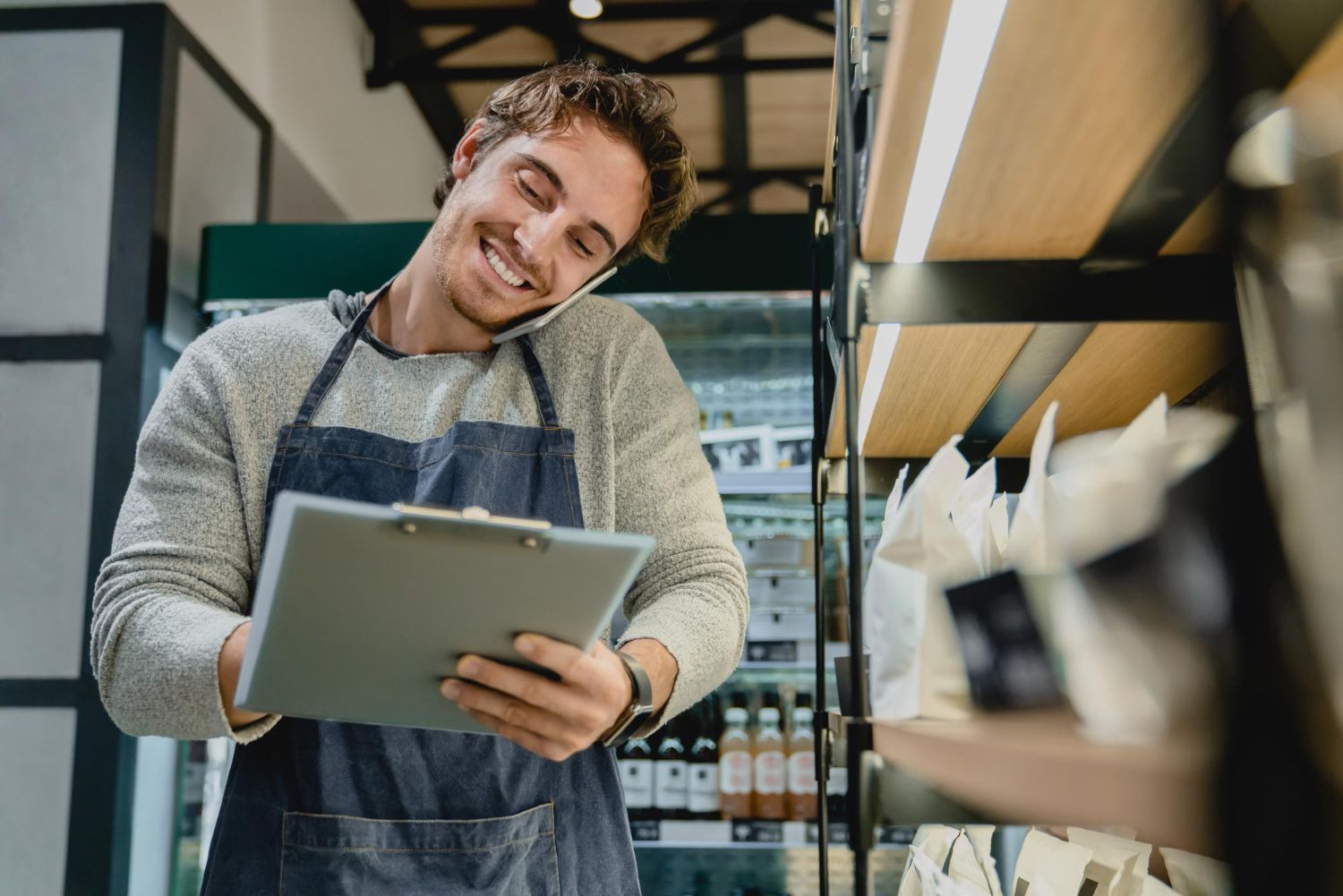 Smiling shop worker in an apron holding a tablet in a grocery aisle