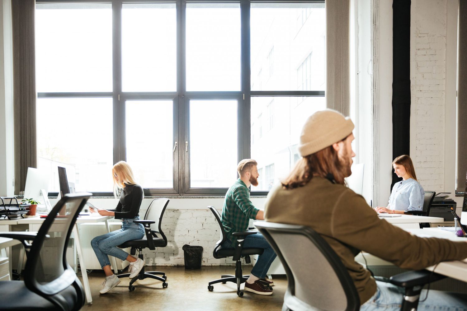 Bright office with people working at desks beside large windows