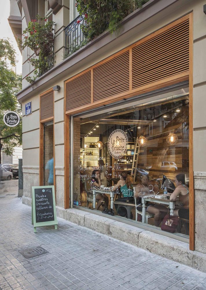Street-level view of a cozy café storefront with wood-trimmed windows and a sidewalk chalkboard menu