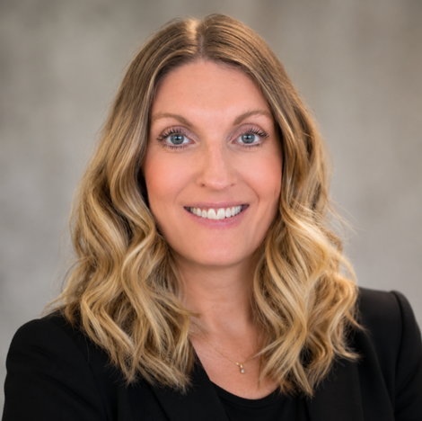 Studio headshot of a smiling woman with wavy blonde hair in a black blazer against a gray background