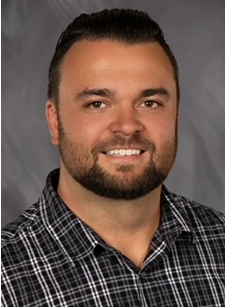 Headshot of a smiling man in a plaid shirt against a gray background