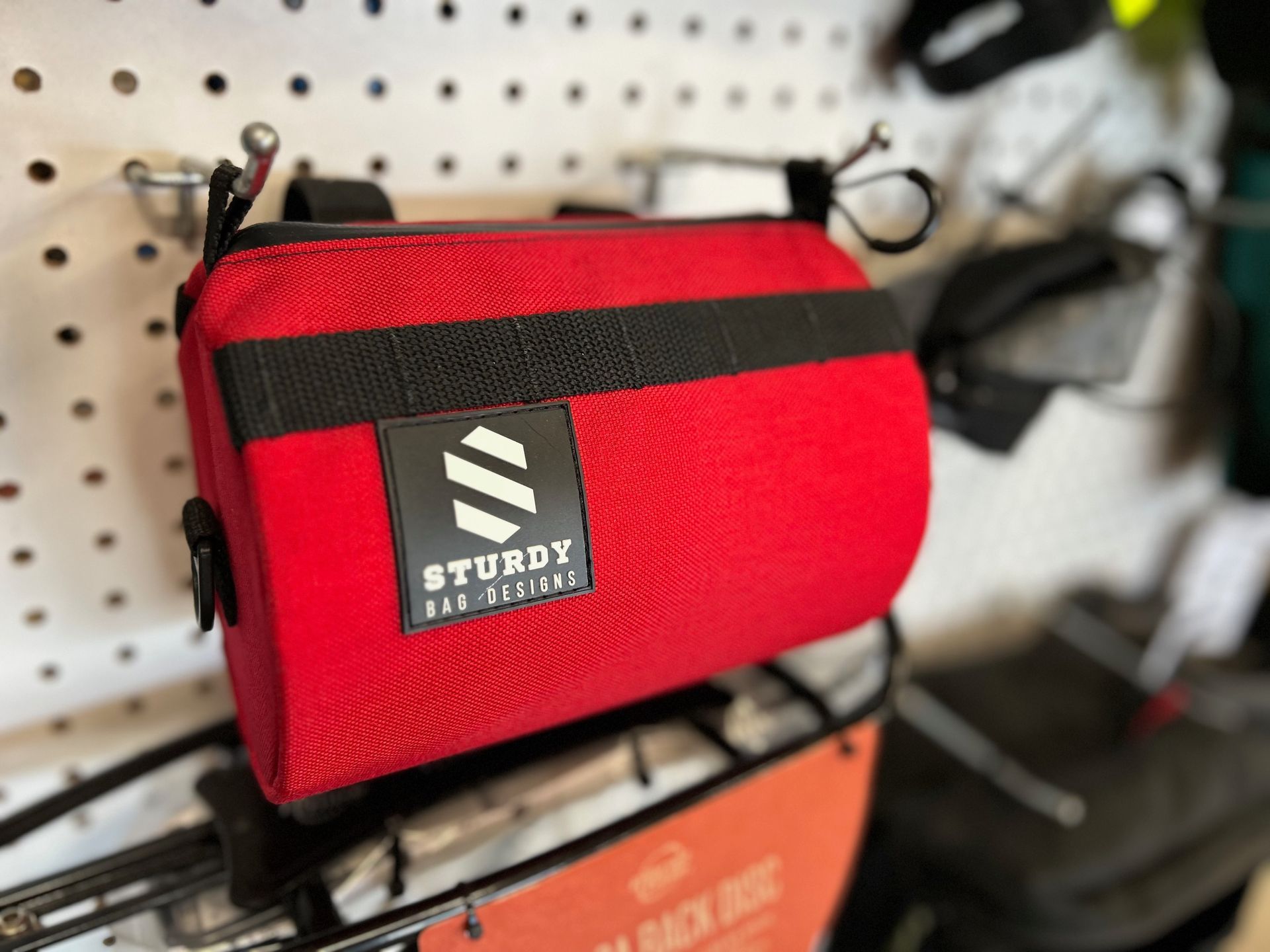 A red bag with a black strap is hanging on a bike rack.