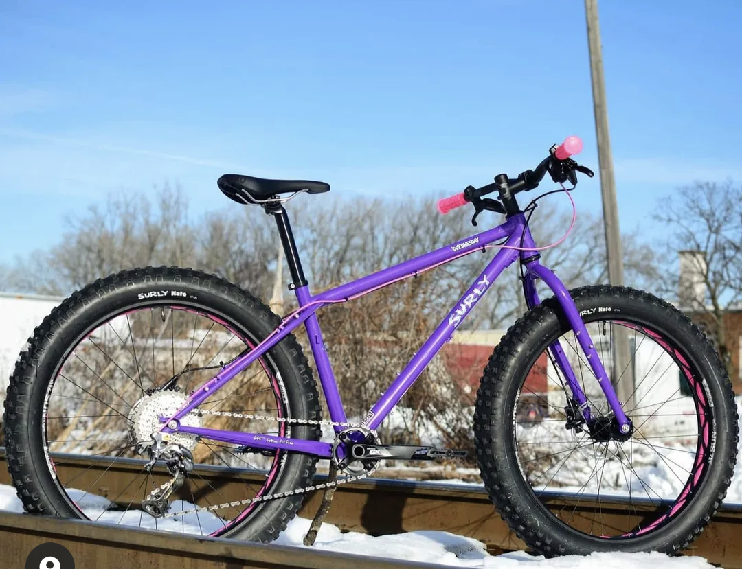 A purple bicycle is parked on a railroad track in the snow.