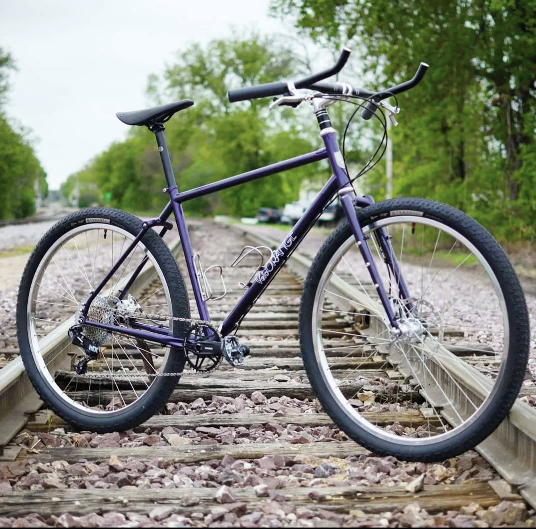A purple bicycle is parked on train tracks