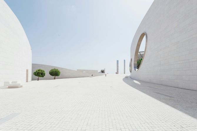 Sunlit white courtyard with curved walls, trees, and a circular window opening