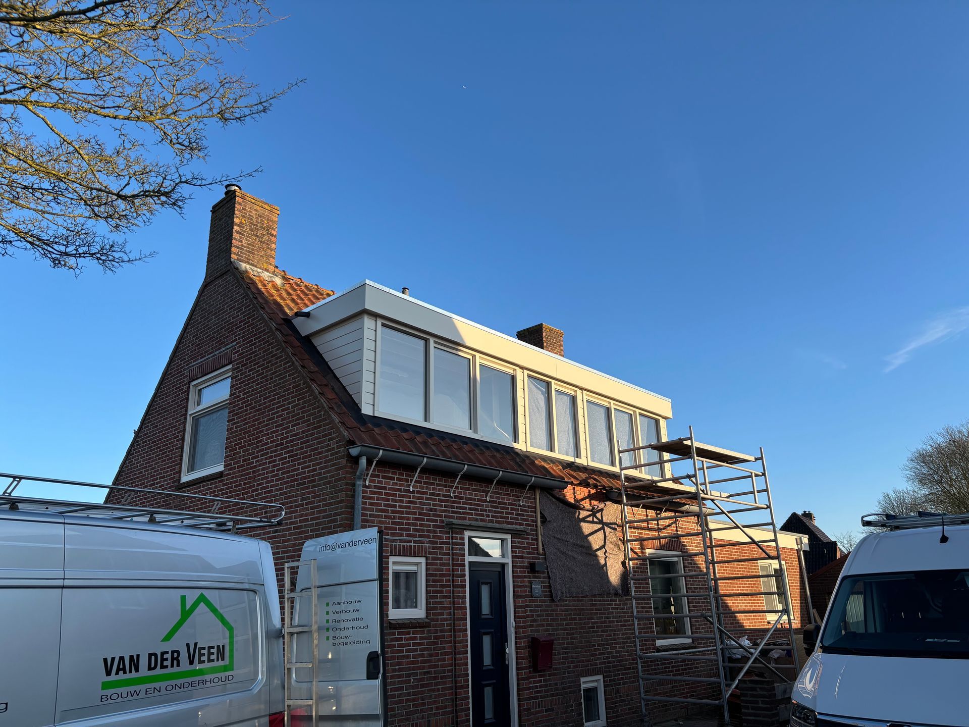 Een bakstenen huis met steigers en een witte bestelwagen onder een helderblauwe hemel.