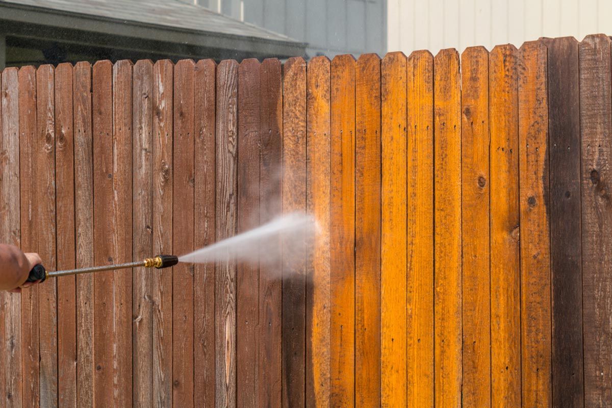 Pressure washing a wooden fence, revealing clean, lighter wood.