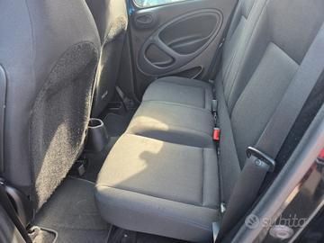 Interno posteriore di un'auto rossa con sedili in tessuto nero, cuciture bianche e cinture di sicurezza.