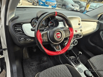 Vista interna di una Hyundai i10, che mostra il cruscotto, il volante, i sedili e la leva del cambio. Il cruscotto ha un inserto blu.