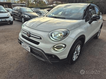 Hyundai i10 argentata parcheggiata su un piazzale ghiaioso, con altre auto sullo sfondo. Ripresa diurna, cielo nuvoloso.