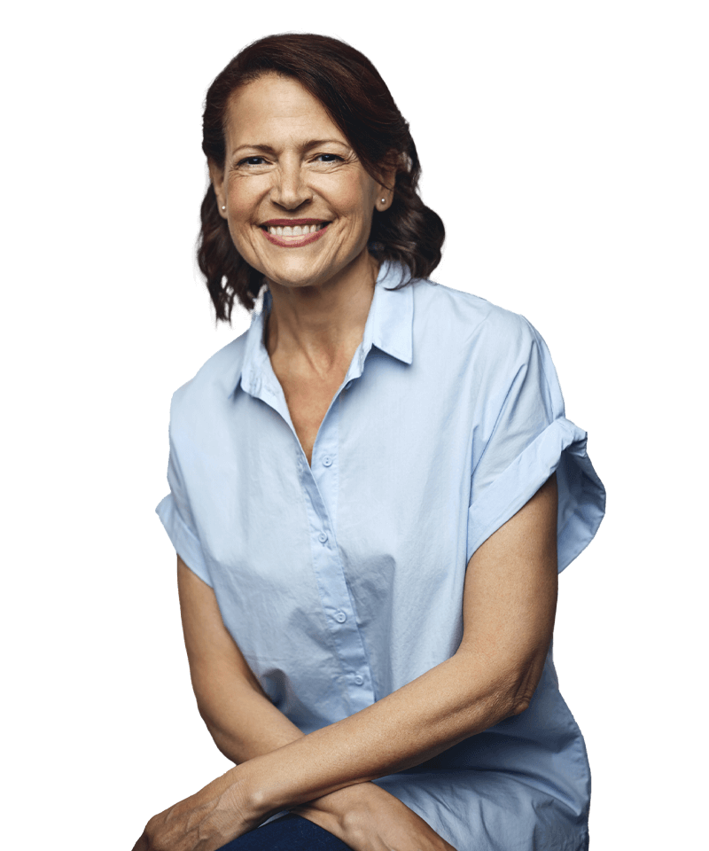 A woman in a blue shirt is sitting with her legs crossed and smiling.
