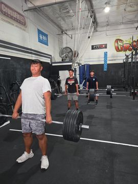 A large group of people smiling and posing in a gym with weightlifting equipment in the foreground.