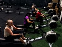 An instructor leads a workshop for a seated group in a gym with CrossFit branding on the wall.