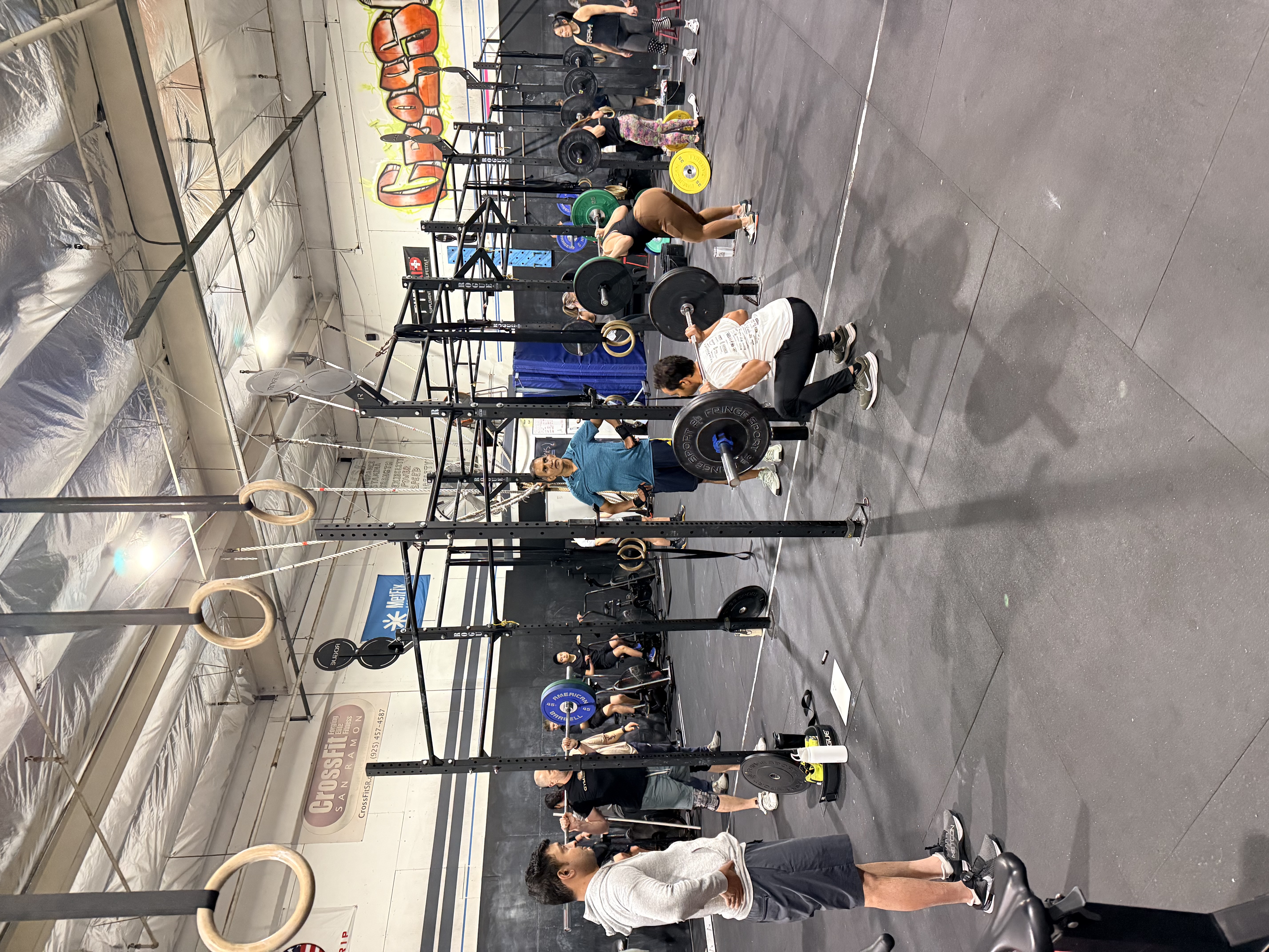 A group of eleven people standing and posing together in a CrossFit gym, one person crouching in the front center.