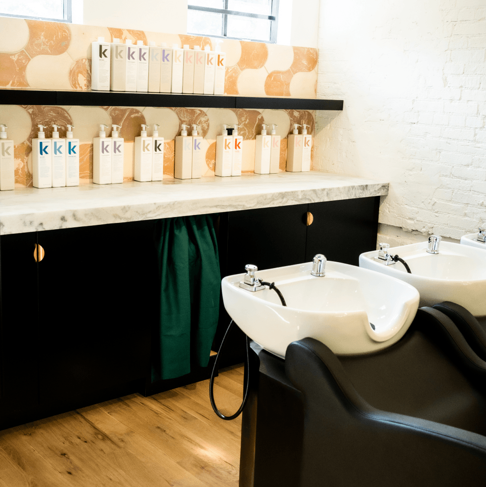A hair salon with two sinks and a shelf with bottles of shampoo on it.