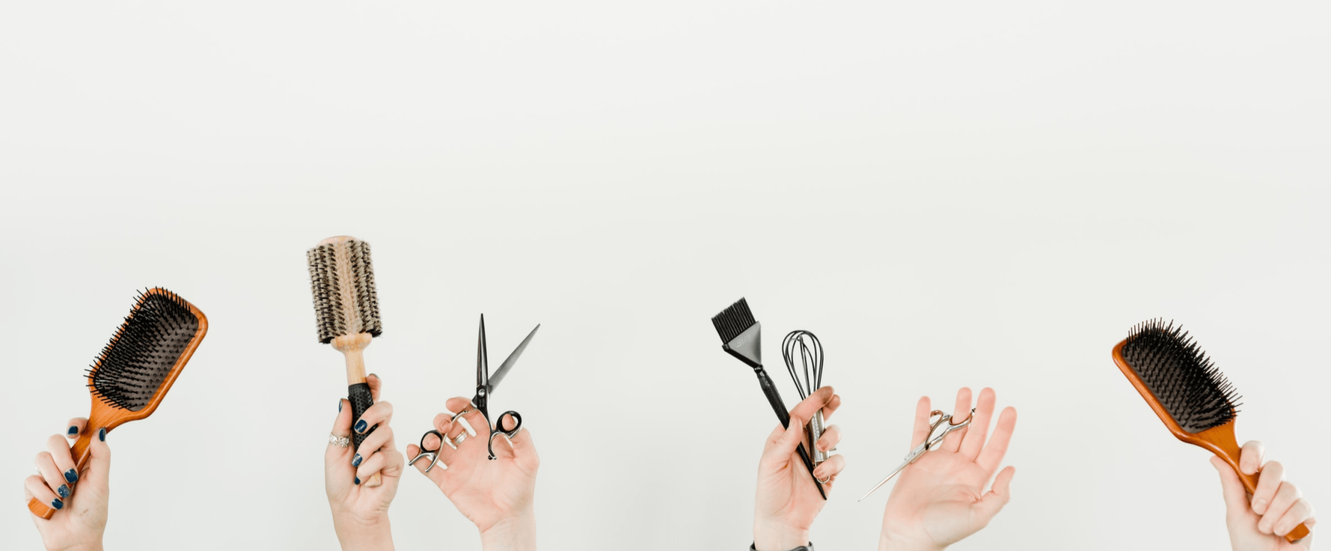 A group of people are holding up hair brushes , scissors , and combs.