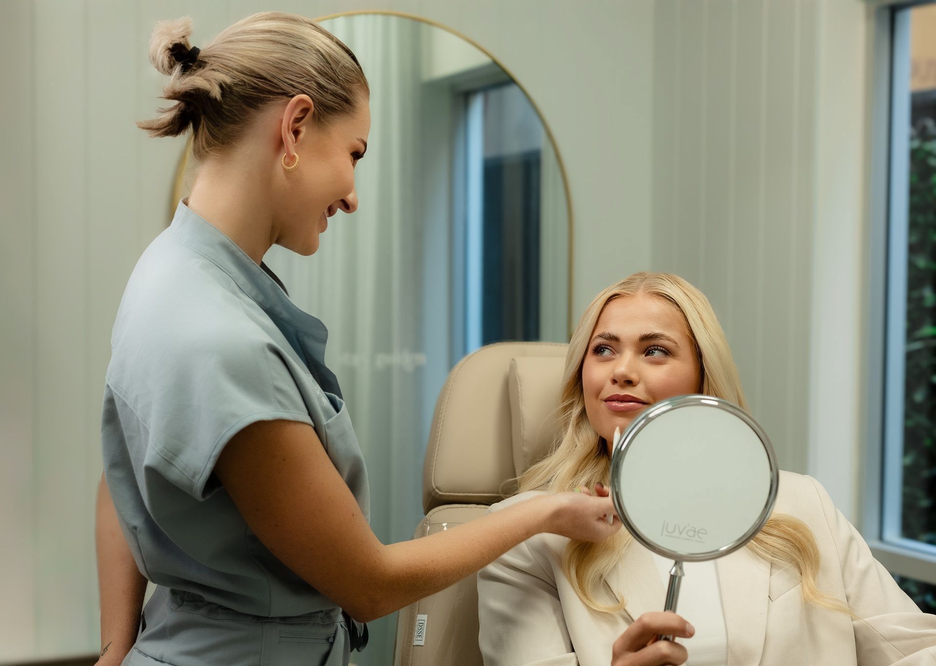 Woman receiving cosmetic treatment, looking in a mirror in a medical office.