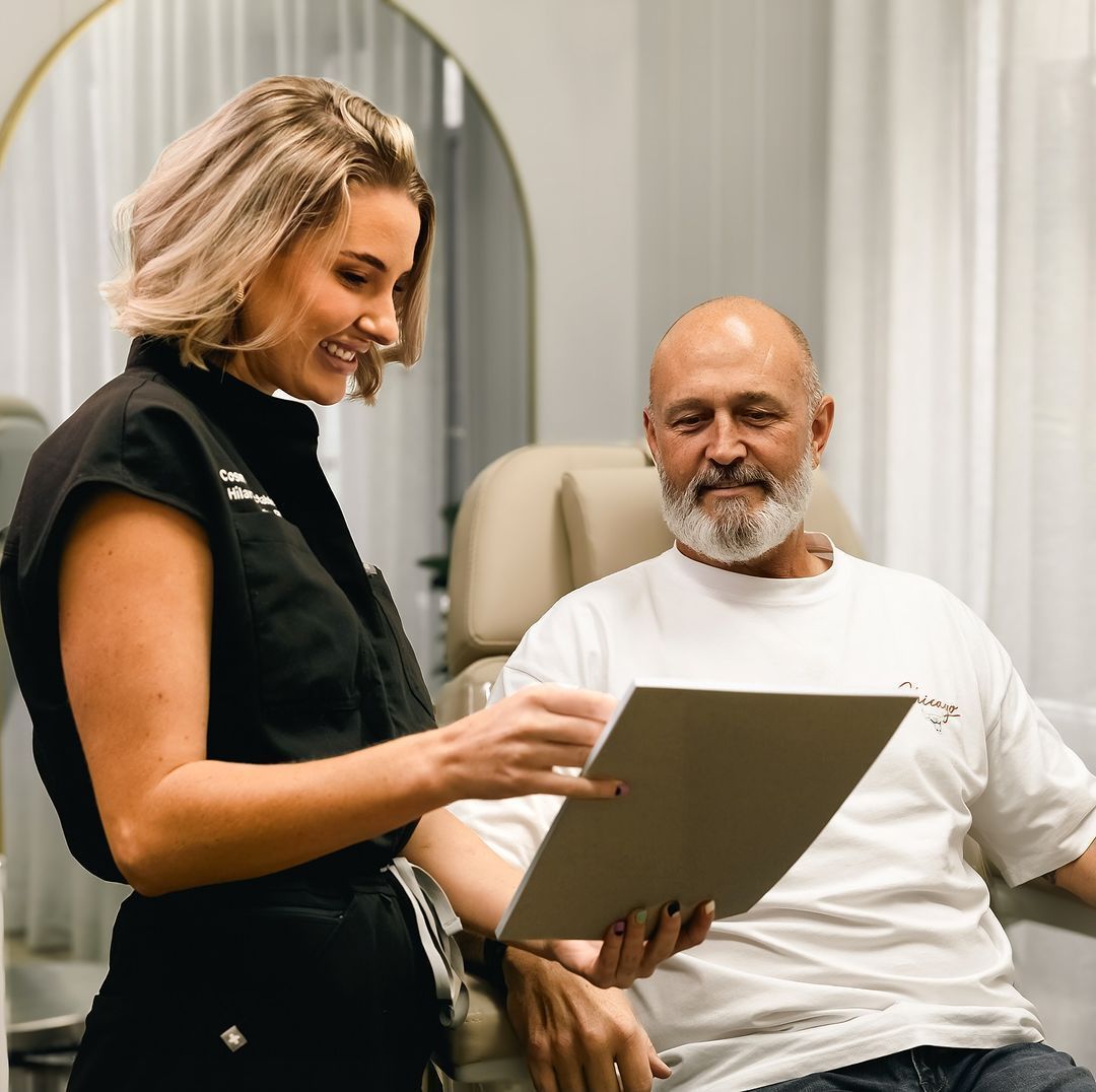 Woman in black uniform showing paperwork to a seated man in a white shirt. Beige interior.
