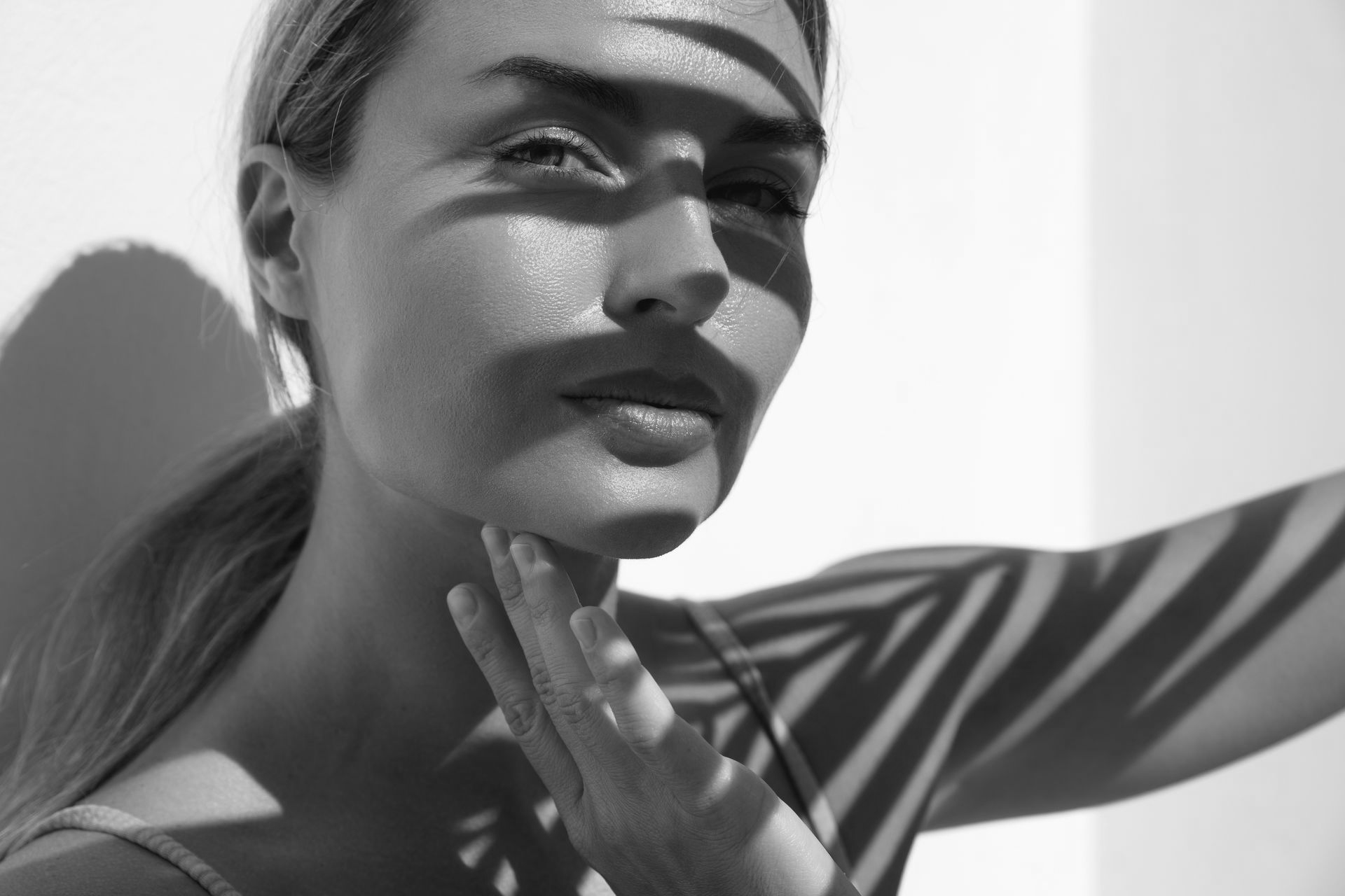 Woman with hand on chin, face partially shaded by palm fronds, in black and white.