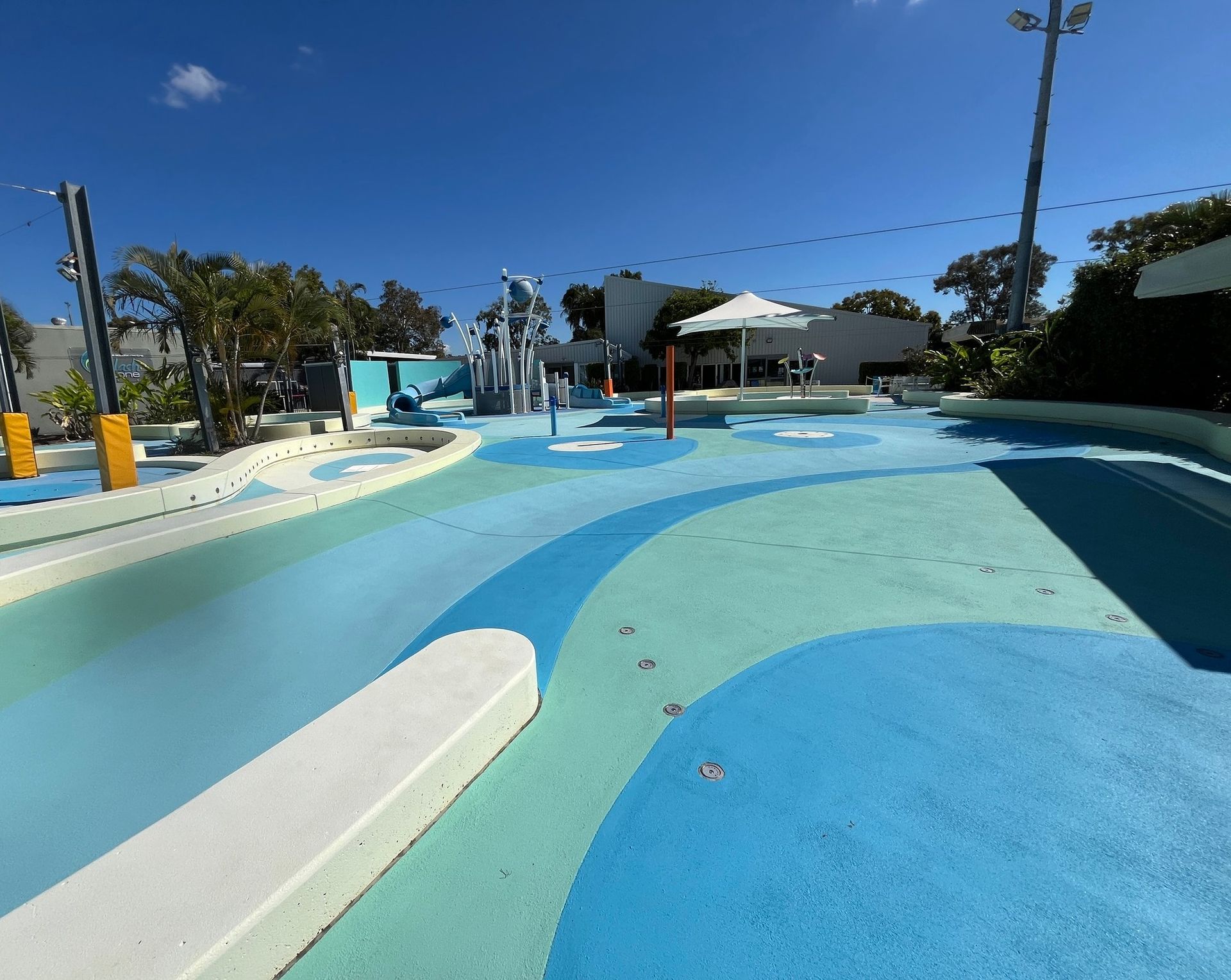 An Empty Outdoor Water Play Area With a Blue and Light Green Ground — Priority Painters in Gladstone Central, QLD