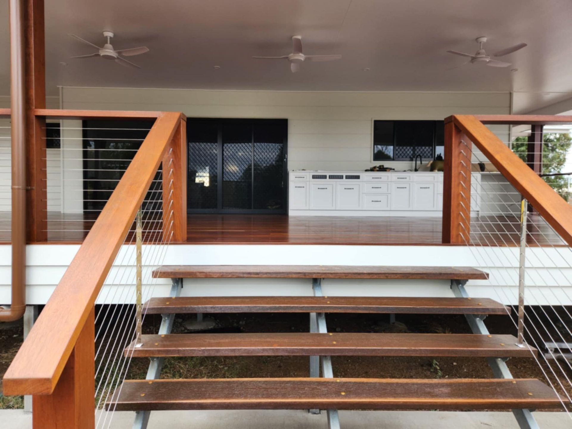 Wooden Stairs Lead Up to a Covered Outdoor Deck Featuring a White Cabinet — Priority Painters in Gladstone Central, QLD