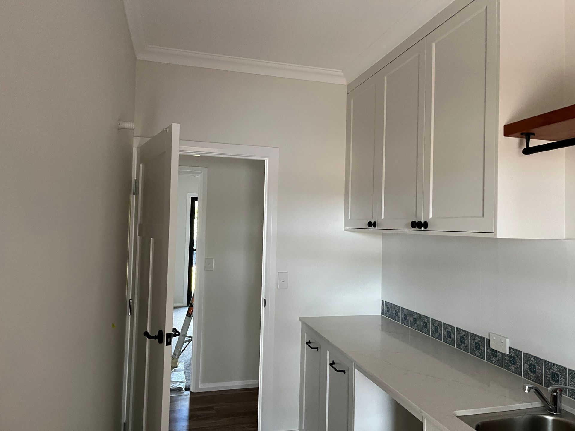 A White-toned Kitchen Area With White Cabinetry, a Sink, Patterned Backsplash — Priority Painters in Gladstone Central, QLD