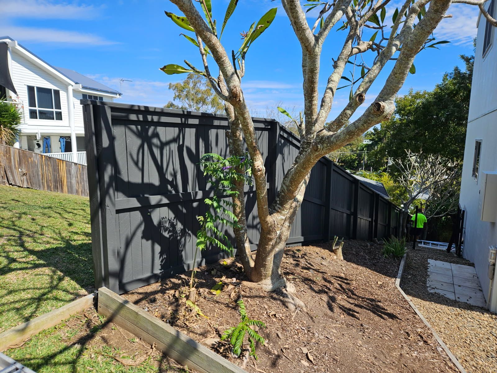 A Black Wooden Fence Descends a Sloped Yard Next to a White House — Priority Painters in Gladstone Central, QLD