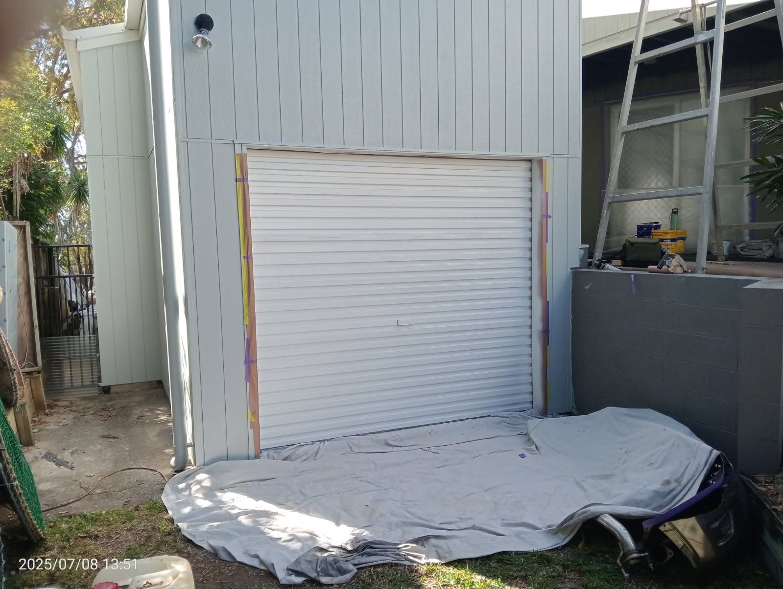 A Light Blue Exterior Wall With a White Roll-up Garage Door — Priority Painters in Gladstone Central, QLD
