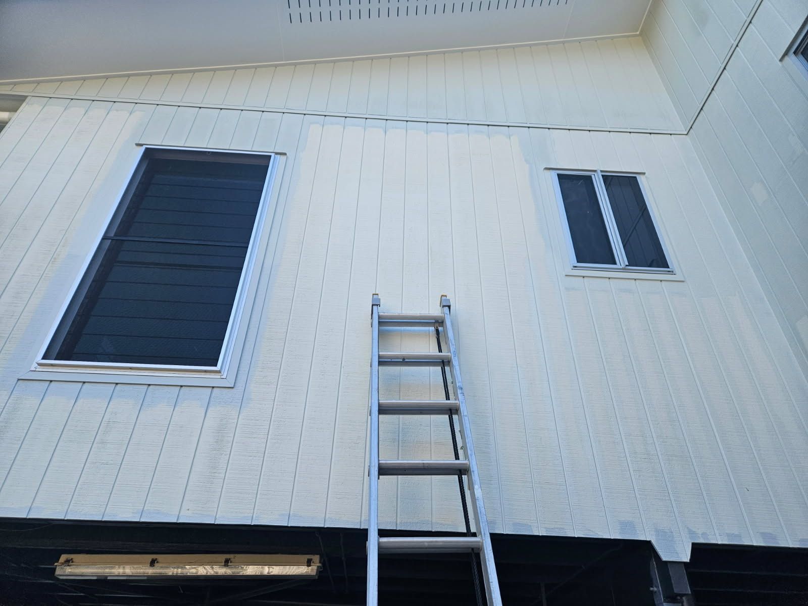A Metal Ladder Leaning Against the White-paneled Exterior Wall — Priority Painters in Gladstone Central, QLD
