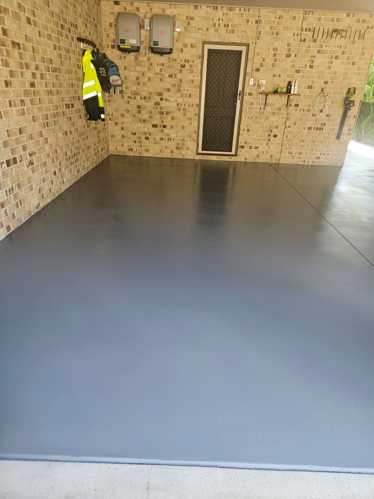 A Freshly Painted, Smooth Gray Concrete Garage Floor With a Brick Wall — Priority Painters in Gladstone Central, QLD