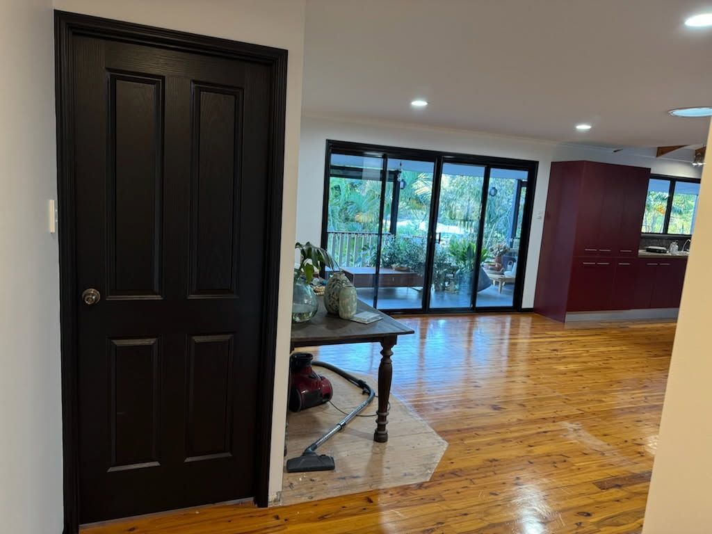 A Black Interior Door Stands in a Room With Polished Wooden Floors — Priority Painters in Gladstone Central, QLD