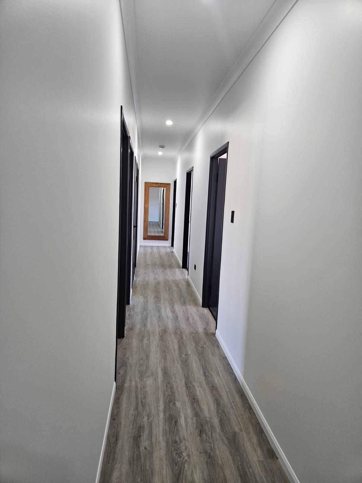 A Hallway With White Walls, Wood-look Flooring, and Several Dark Doors — Priority Painters in Gladstone Central, QLD