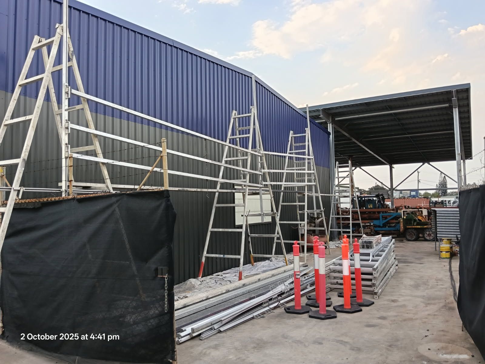 Three Tall Metal Ladders Lean Against the Dark Blue Wall — Priority Painters in Gladstone Central, QLD