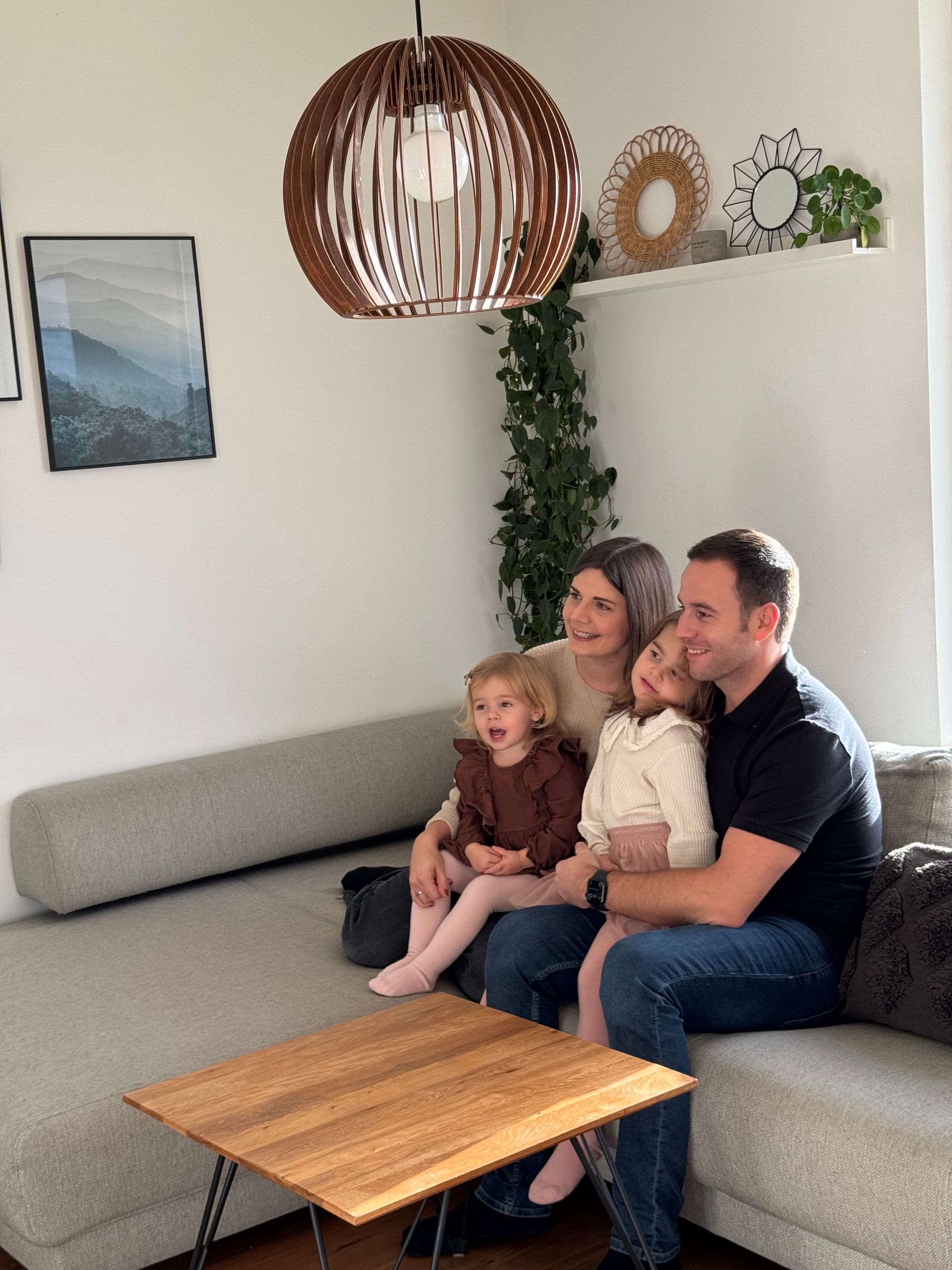 Eine vierköpfige Familie sitzt auf einem grauen Sofa in einem hellen Wohnzimmer.