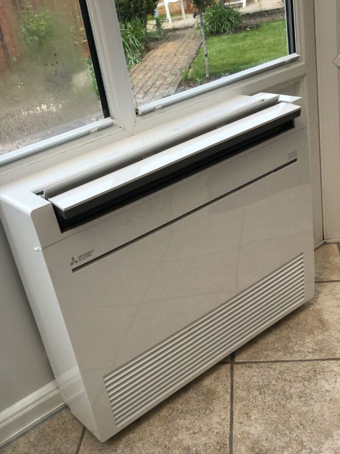 White Mitsubishi air conditioning unit near a window, set on tiled floor.