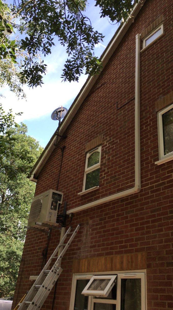 Brick building exterior with white pipes and air conditioning unit. A ladder is leaning against the building.