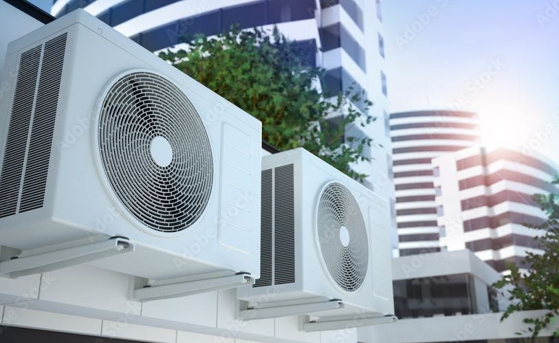 Air conditioning units mounted on a building exterior with skyscrapers in the background.