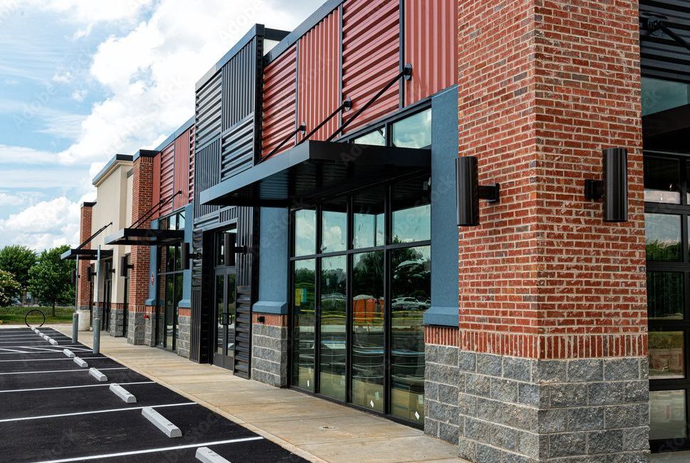 Strip mall storefront with brick and corrugated metal facade, awnings, and large windows.