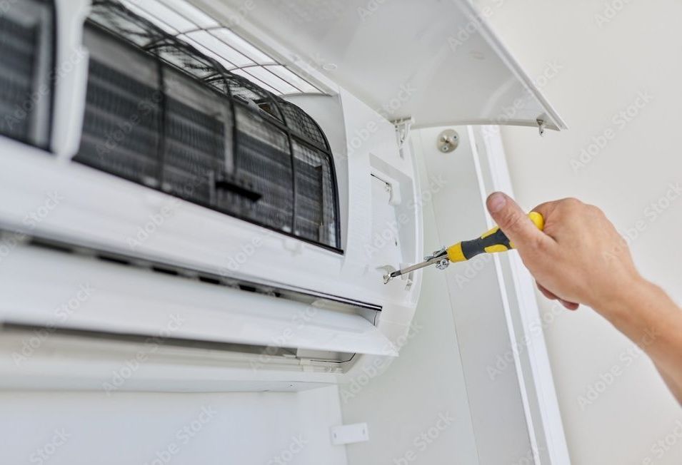 Person using a screwdriver to open a white air conditioning unit.