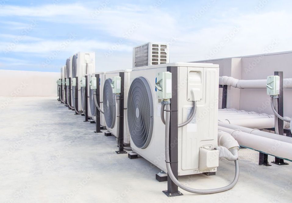 Row of air conditioning units on a rooftop, with sky and pipes visible.