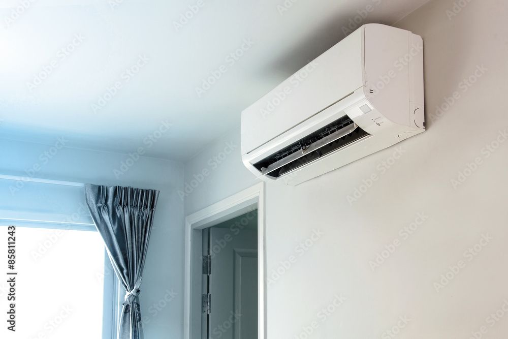 White wall-mounted air conditioner in a room, near a window with curtains and a doorway.