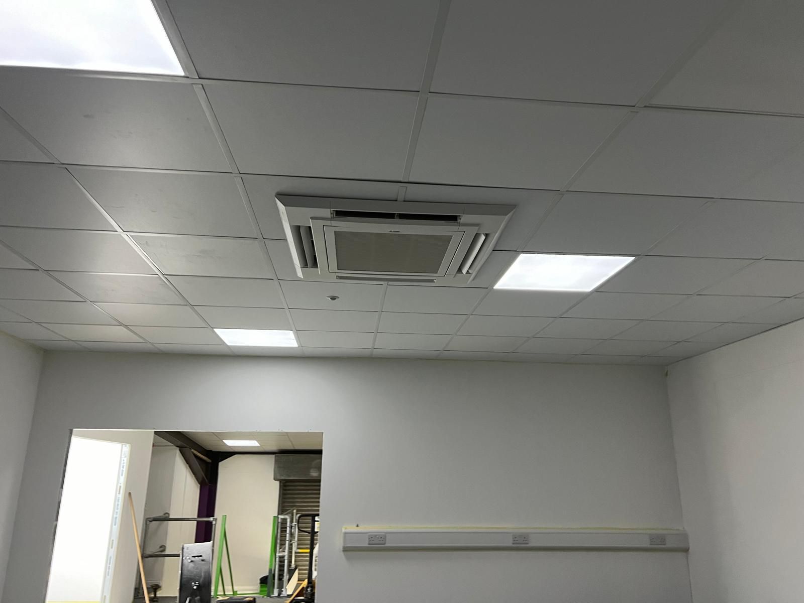 Ceiling with recessed air conditioning unit and square lights in a white-walled room.